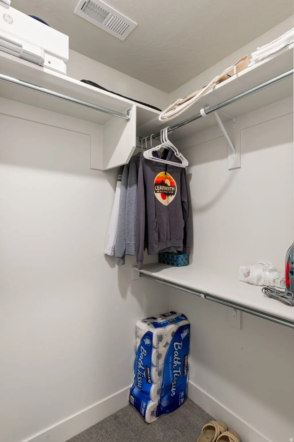 Recessed closet featuring white walls, white shelving, metal hanging rods, white trim, and light gray carpet flooring