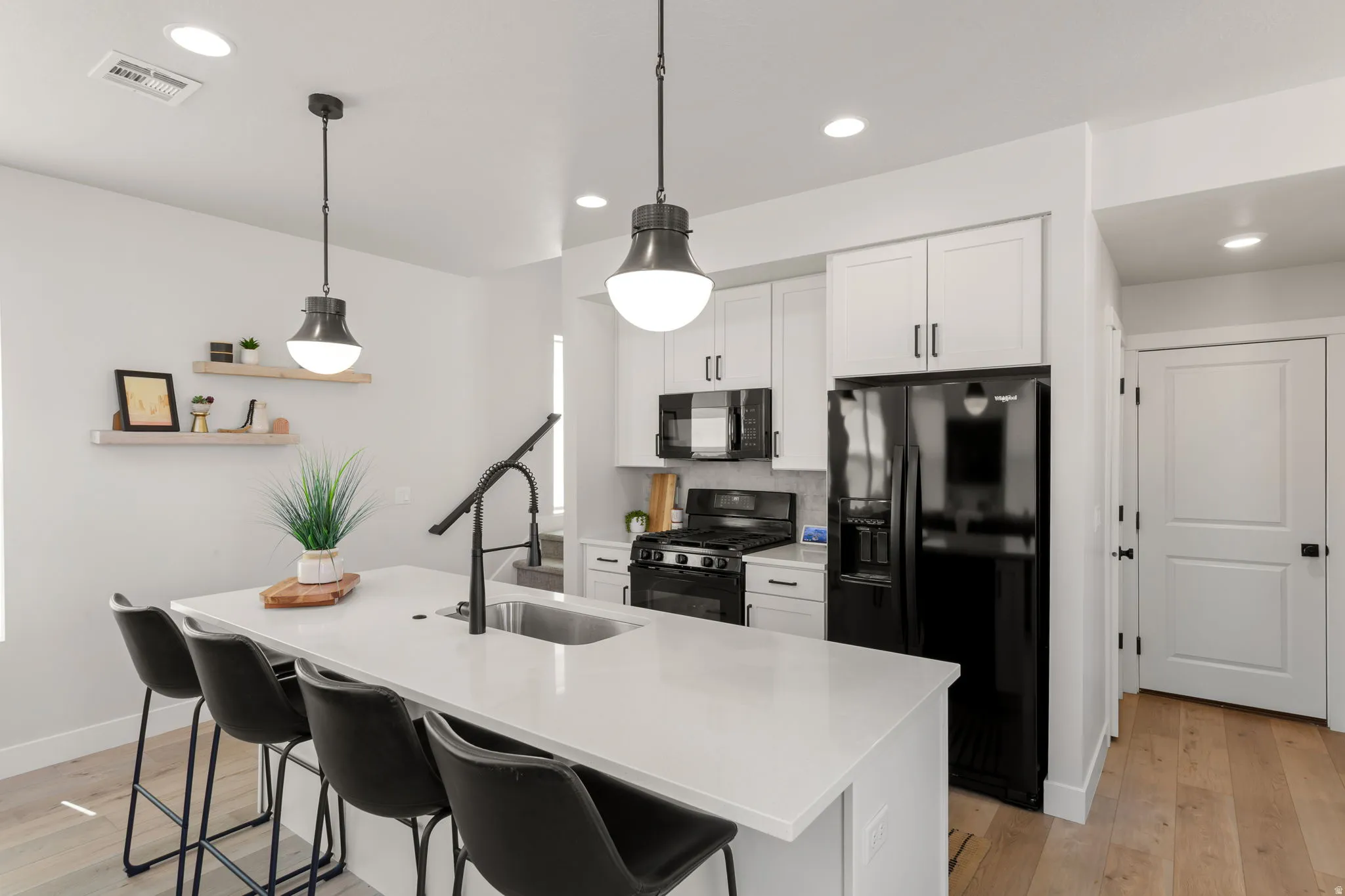 Kitchen featuring a center island with sink and seating, white cabinetry, black appliances, and pendant lighting