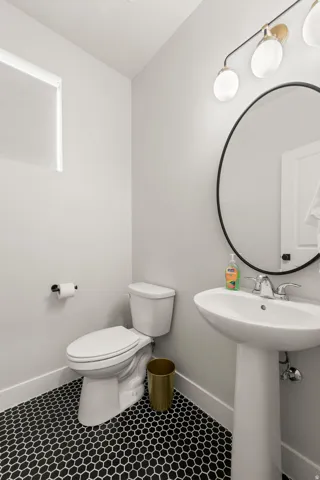 Pedestal sink with chrome faucet, complemented by a large circular mirror and a three-light vanity fixture
