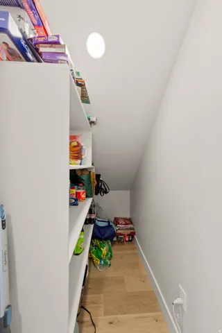Pantry featuring built-in shelving, wood-finish flooring, and sloped ceiling