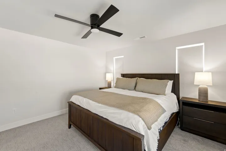 Bedroom featuring light gray carpeting, crisp white walls, a black ceiling fan, and recessed window openings