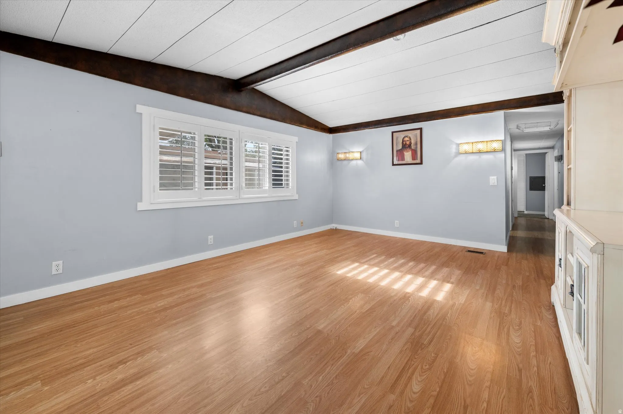 Spacious interior room featuring wood-finish flooring, white baseboards, and a light blue wall color