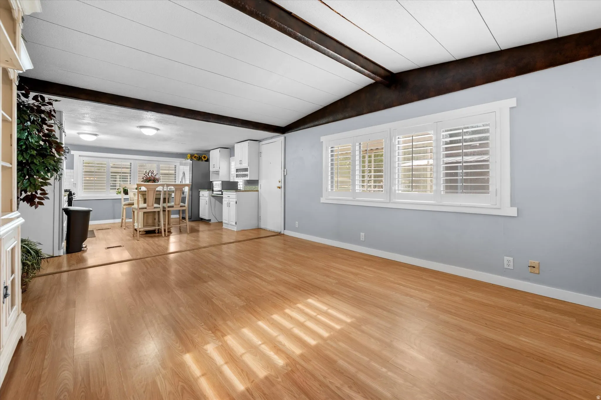 Open-concept living space featuring wood-finish flooring, exposed ceiling beams, and white plantation shutters
