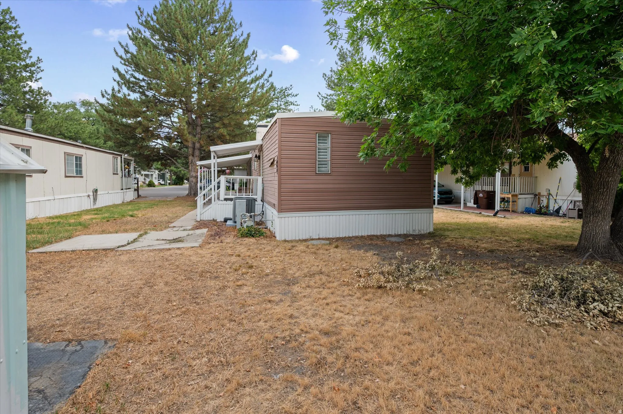 Brown siding with white trim, featuring a side deck with white railings and an exterior cooling unit