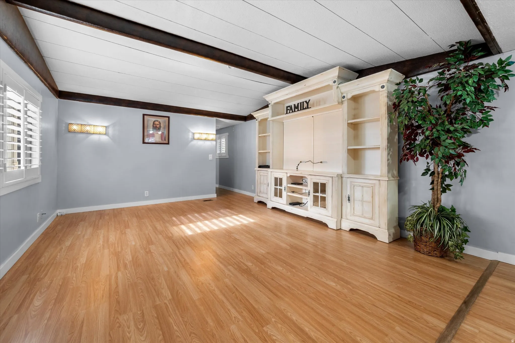 Spacious living area featuring wood-finish flooring, a decorative ceiling with exposed beams, and light blue walls