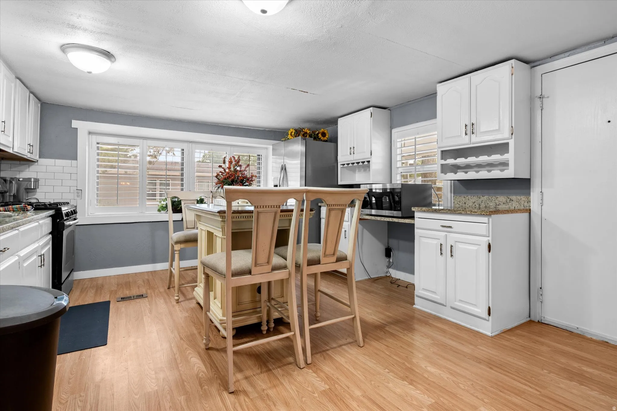 Kitchen featuring an island with seating, wood-finish flooring, white cabinetry, and light-toned countertops
