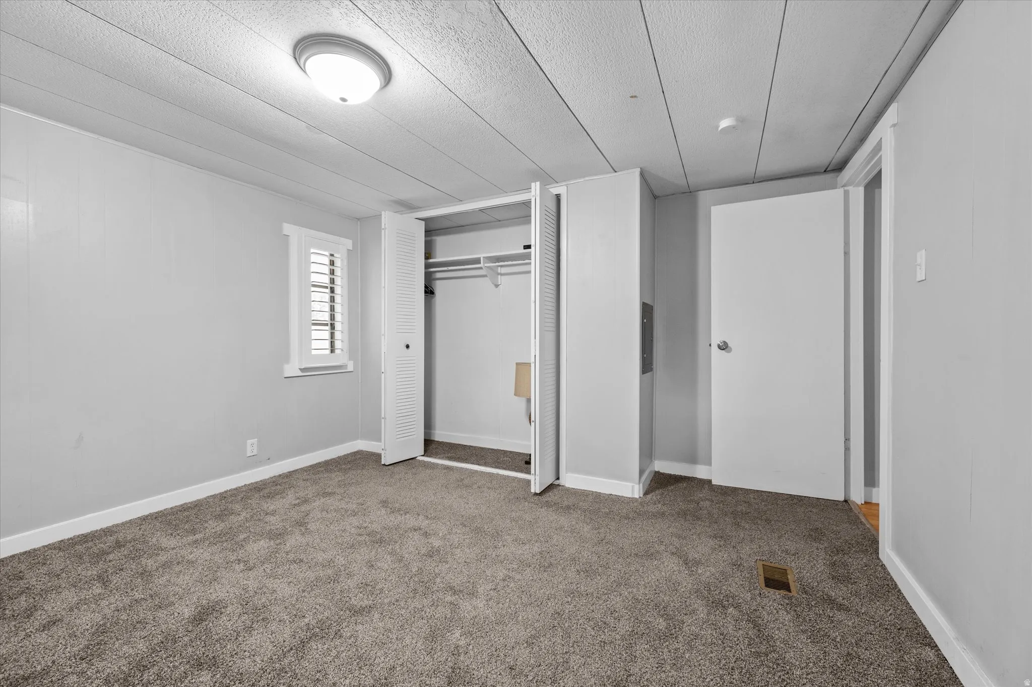 Neutral-toned room featuring a window with white louvered shutters, wall-to-wall carpeting, and a bi-fold door closet with built-in hanging rods