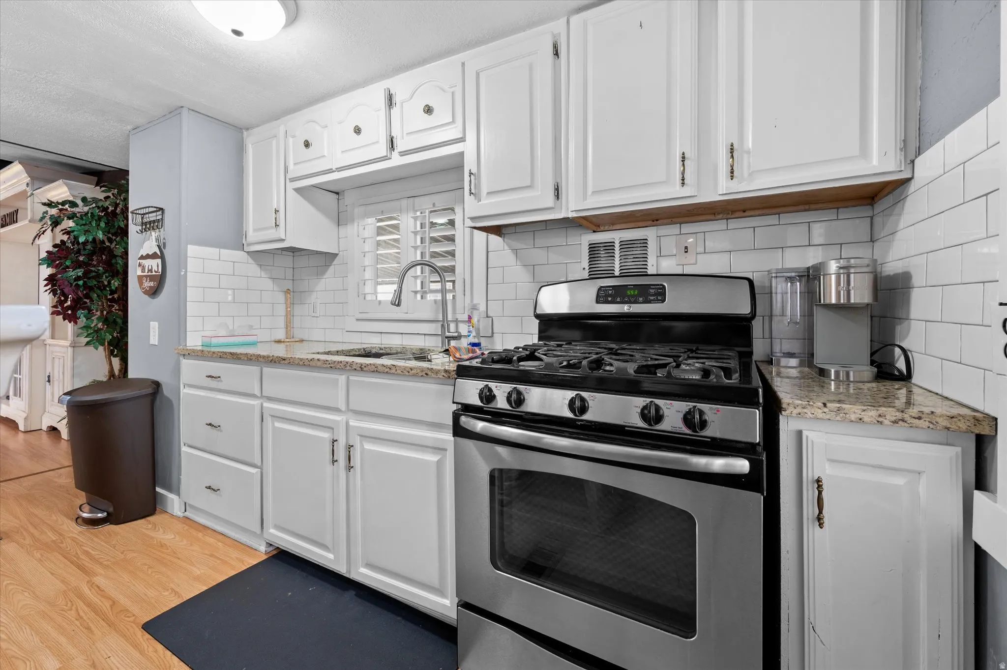 Kitchen featuring white cabinetry with brushed nickel hardware, a stainless steel gas range, and light-toned granite countertops