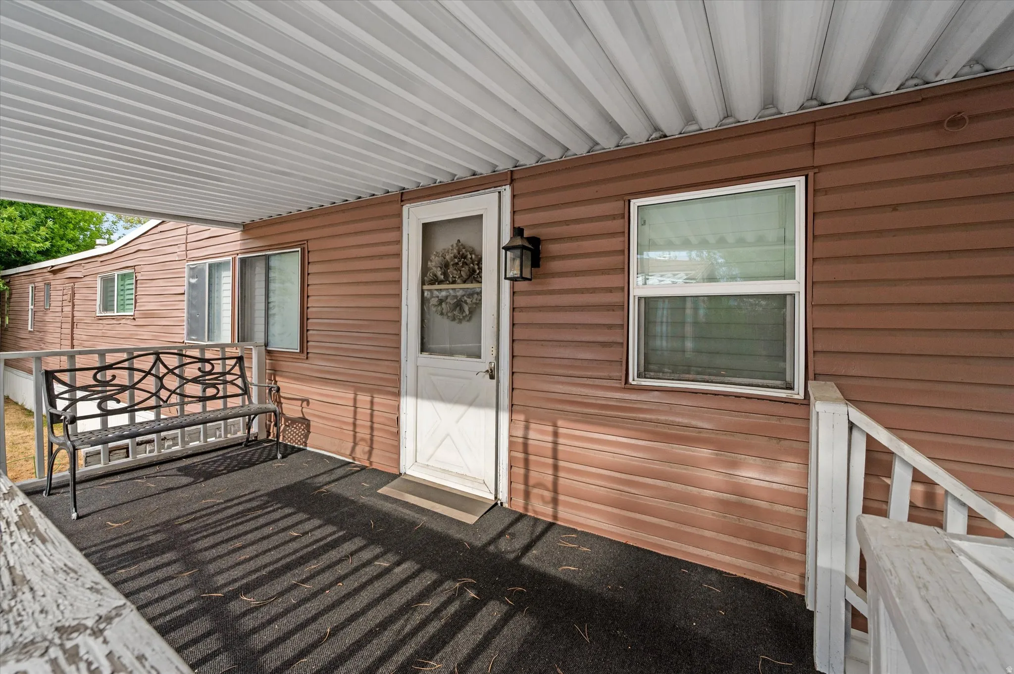 Covered porch entry featuring a white screen door, exterior wall lantern, and horizontal brown siding