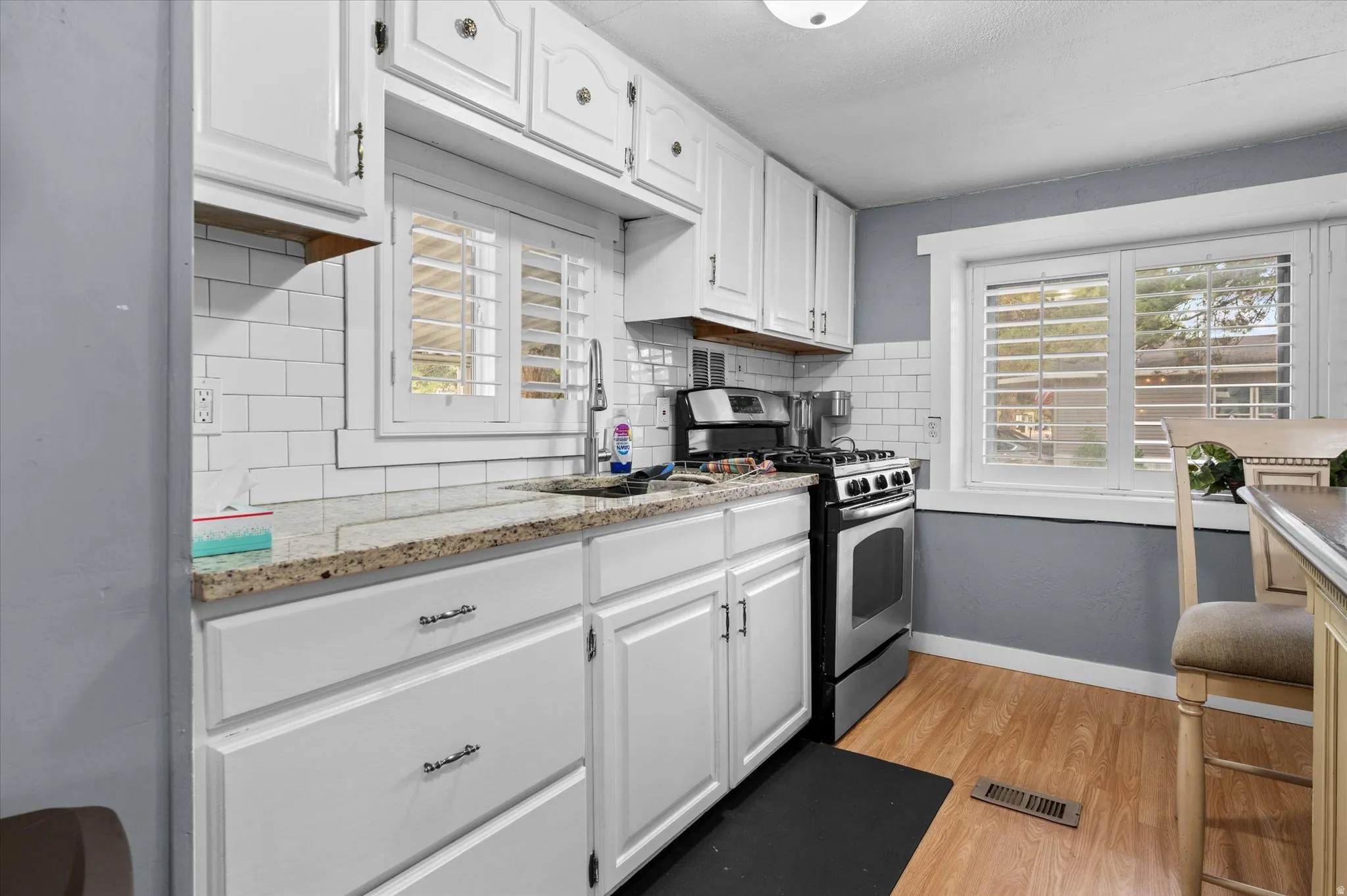 Kitchen featuring white cabinetry, granite countertops, white subway tile backsplash, and wood-finish flooring