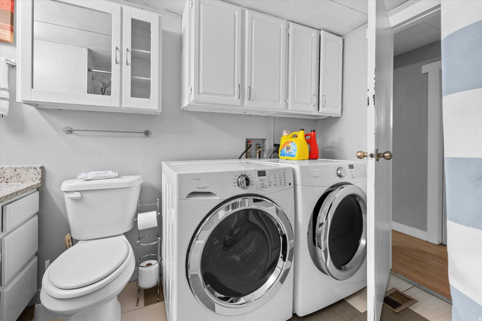 Laundry area with stacked upper cabinetry, a mounted wall cabinet with glass-front doors, and a built-in toilet