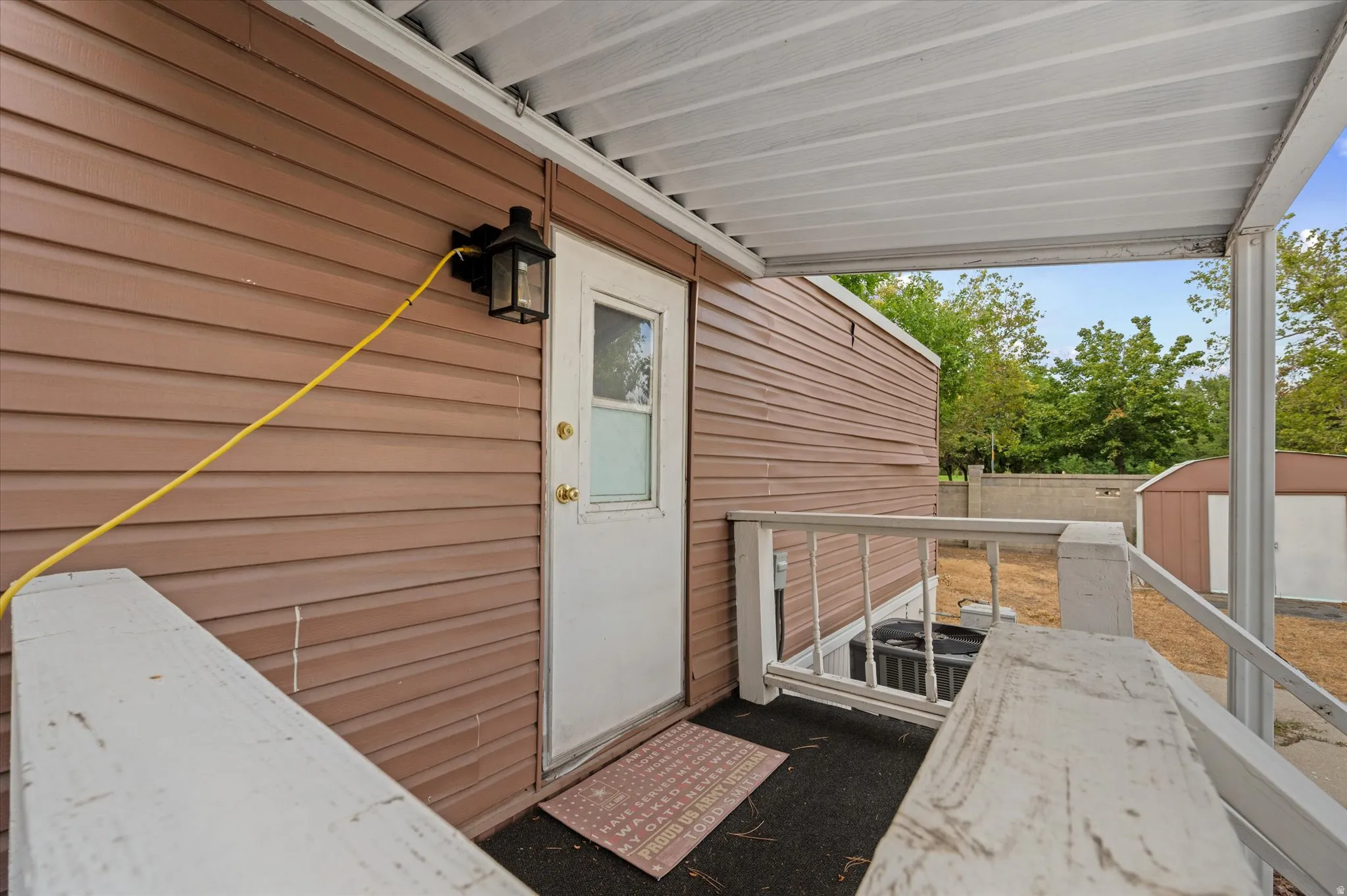 Covered porch entry featuring a white door with a clear glass insert, brown horizontal siding, and a black exterior light fixture