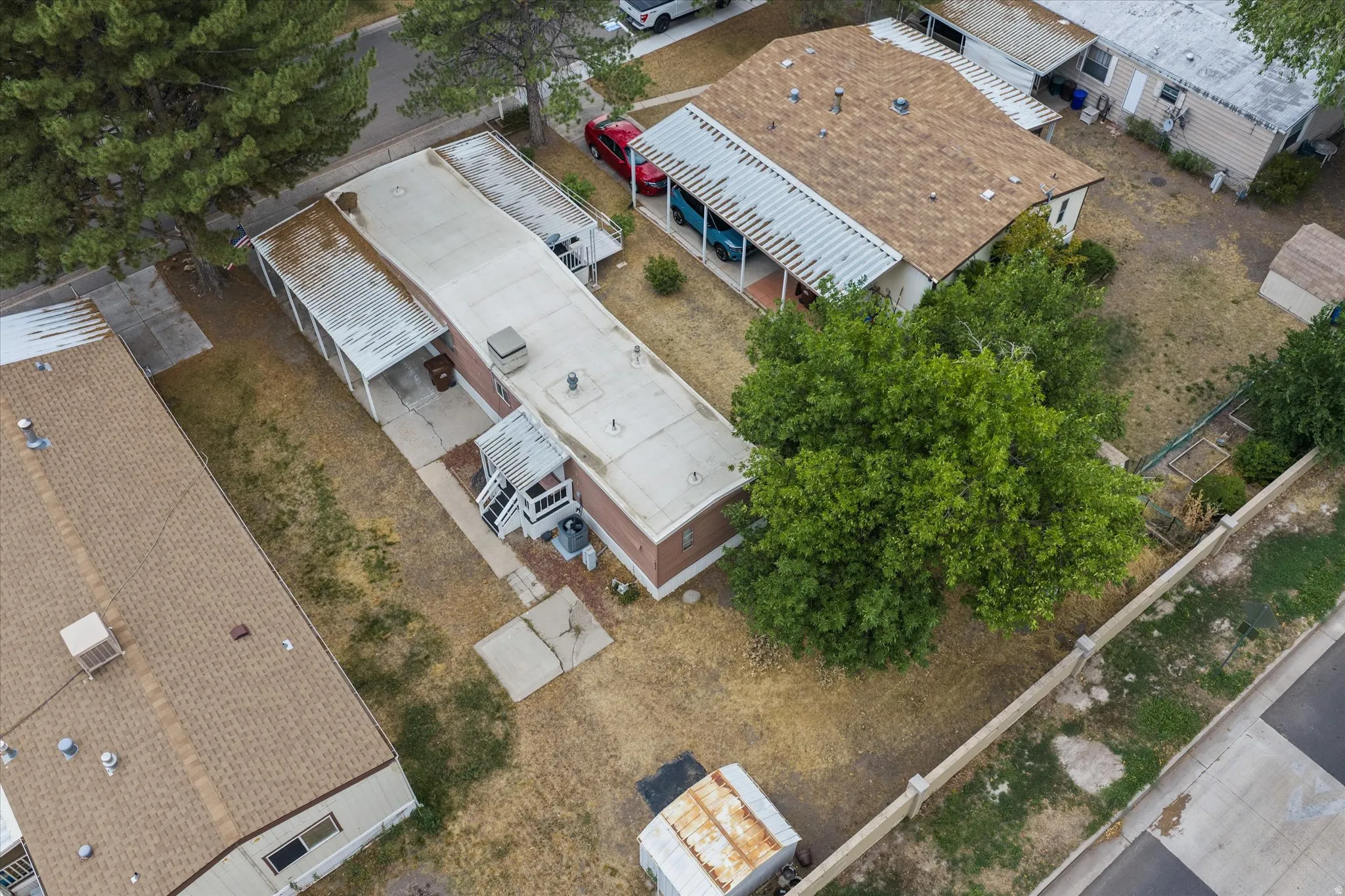 Expansive property featuring a brick exterior, multiple covered parking structures, a mature tree, and a concrete patio