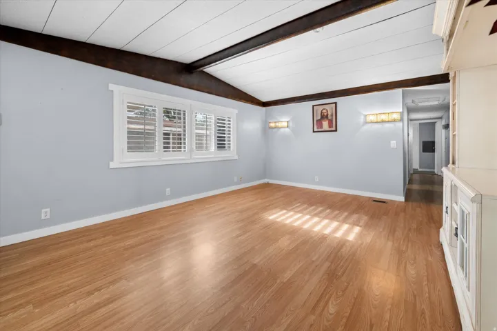 Spacious interior room featuring wood-finish flooring, white baseboards, and a light blue wall color