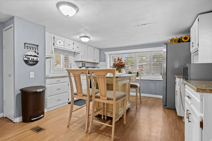 Bright kitchen with wood-finish flooring, white cabinetry, granite-style countertops, and a central island with seating