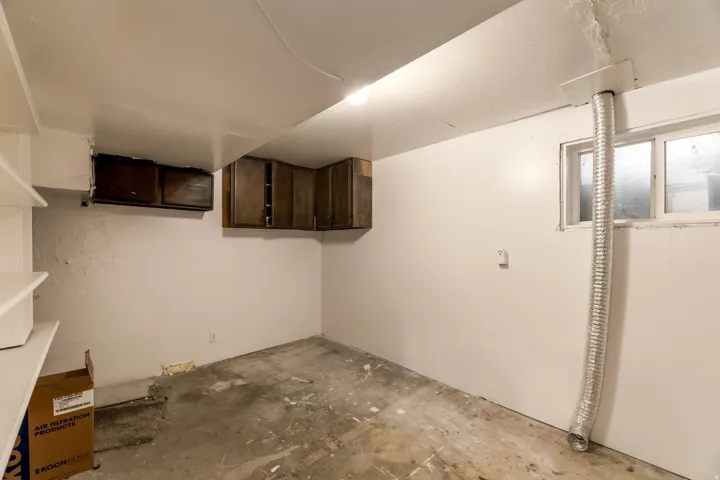 Utility room featuring white walls, concrete flooring, and ample storage with built-in shelving and dark wood-finish cabinetry