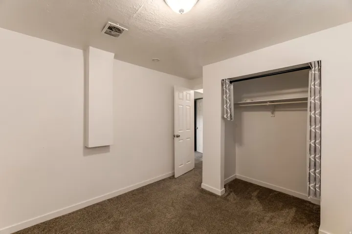 Neutral-toned carpeting and white walls define this interior space, featuring a built-in closet with hanging rod and shelving