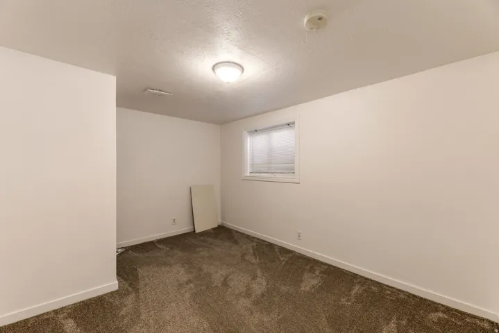 Bedroom featuring neutral-toned carpeting, white walls, and a single window with blinds