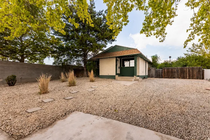 Front exterior featuring a covered porch, gravel landscaping, established trees, and a privacy fence