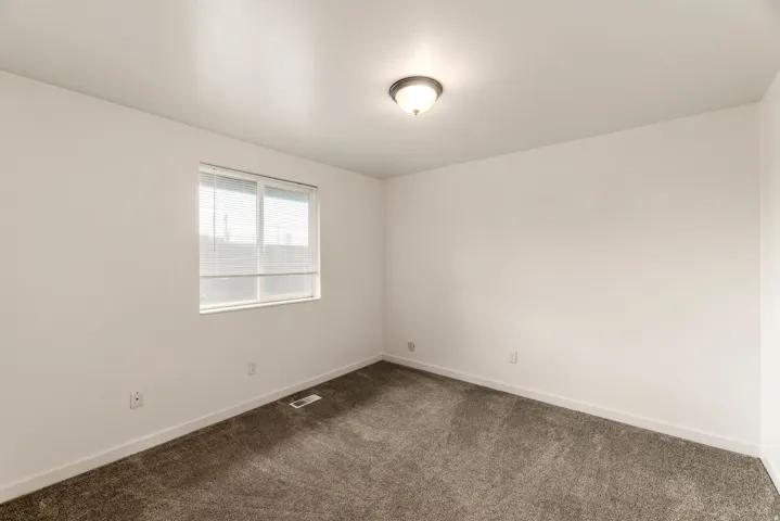 Bright room featuring a double-pane window with horizontal blinds, neutral wall paint, and gray carpet flooring