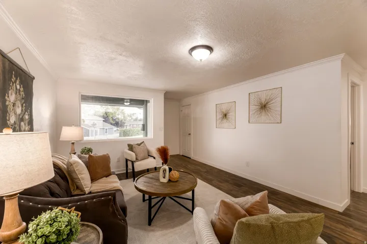 Living area featuring a wide window, crown molding, wood-finish flooring, and white walls