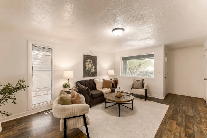 Light-filled living area featuring wood-finish flooring, white walls, and a prominent picture window