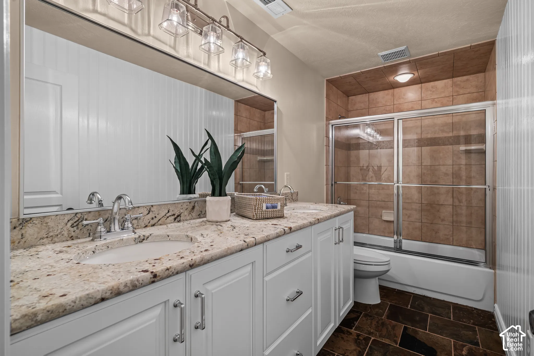 Double vanity with granite countertop, integrated sinks, chrome fixtures, white cabinetry, glass enclosed tub/shower with tile surround