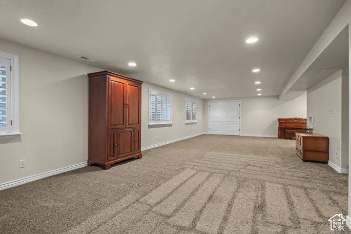 Spacious family room with neutral carpeting, recessed lighting, and multiple windows with white plantation shutters