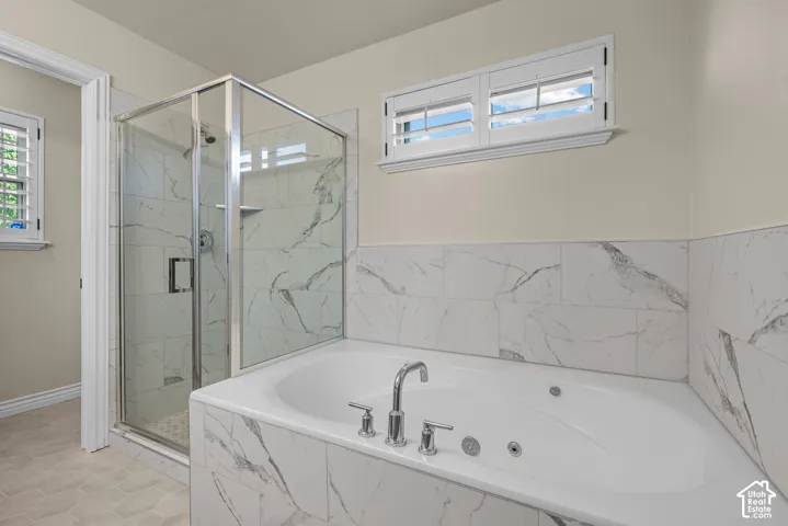 Spa-inspired bath featuring a jetted soaking tub with decorative tile surround, glass-enclosed shower