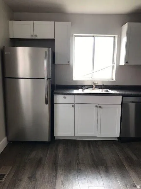 Kitchen featuring white shaker-style cabinetry, dark speckled countertops, stainless steel appliances, and wood-finish flooring