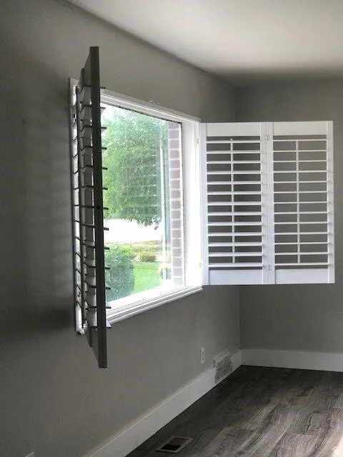 Window featuring white plantation shutters and white trim, complemented by wood-finish flooring, painted walls, and white baseboards