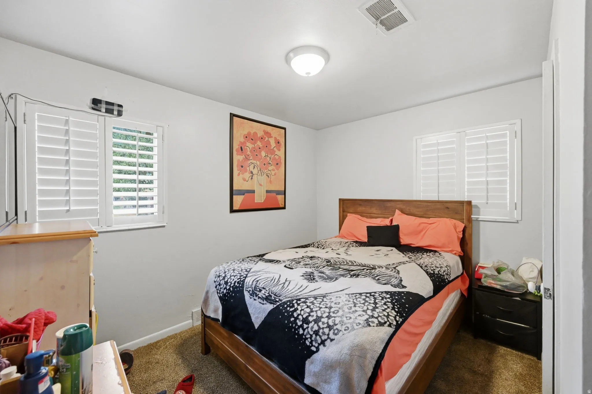Dual windows with plantation shutters, overhead flush mount lighting, and wood-finish bed frame