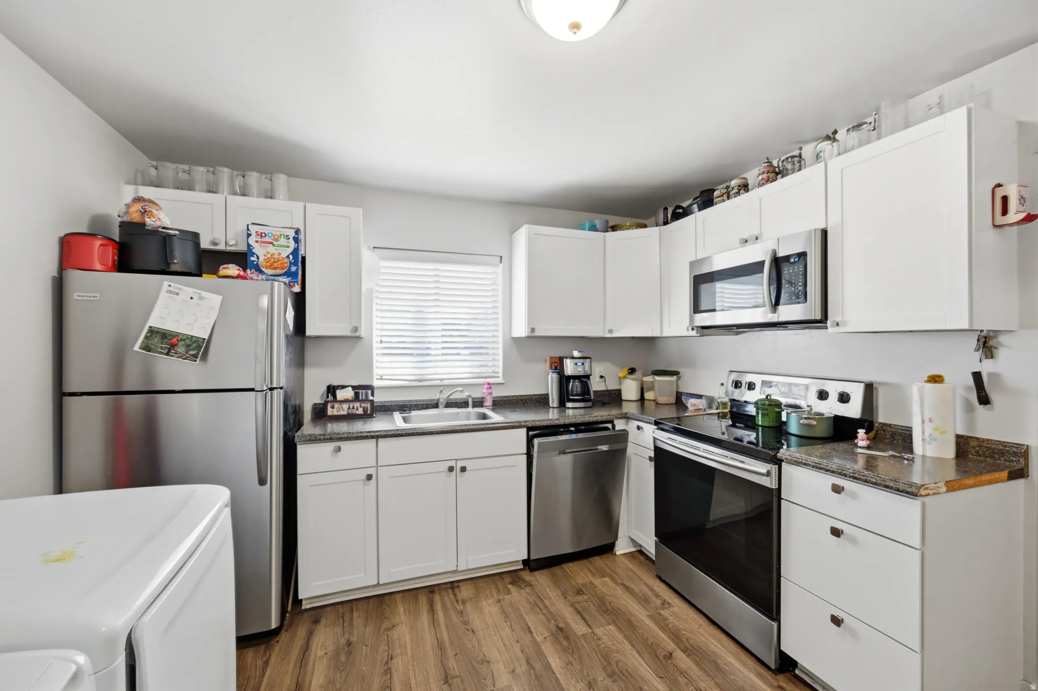 Kitchen featuring white cabinetry, wood-finish flooring, stainless steel appliances, and granite-look countertops