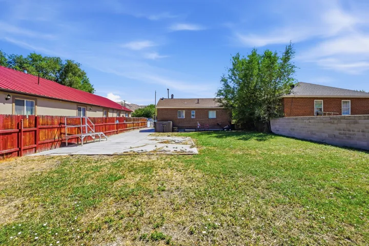Expansive grass yard with concrete patio, wood fencing, and a concrete block retaining wall