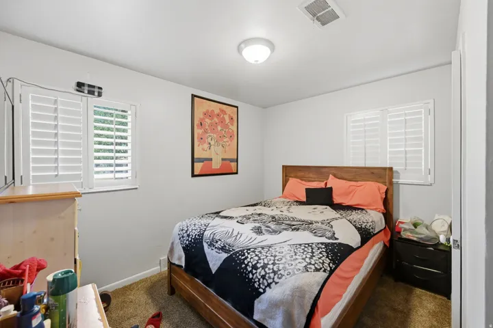 Dual windows with plantation shutters, overhead flush mount lighting, and wood-finish bed frame