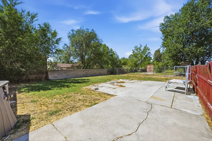 Expansive outdoor space featuring a concrete patio, a section of turf, a concrete block retaining wall, and mature perimeter trees