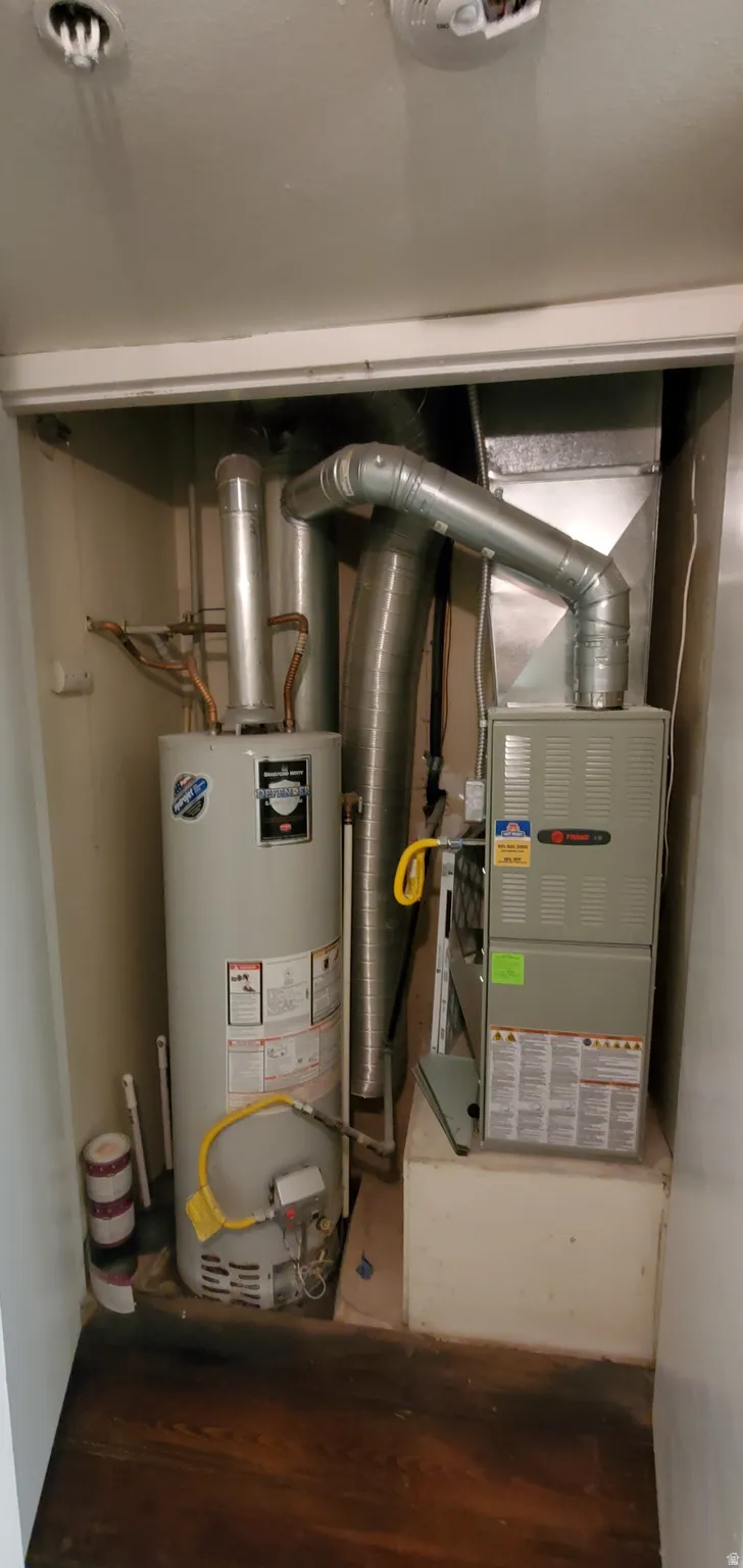 Dedicated utility closet featuring a water heater and furnace with exposed ductwork
