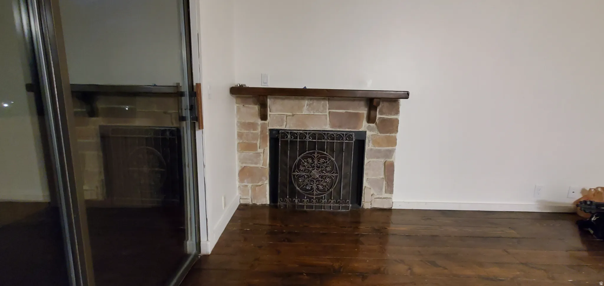 Stone fireplace with an ornate metal screen, dark wood mantel, and rich wood-finish flooring