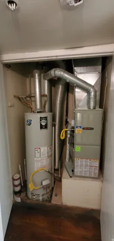 Dedicated utility closet featuring a water heater and furnace with exposed ductwork