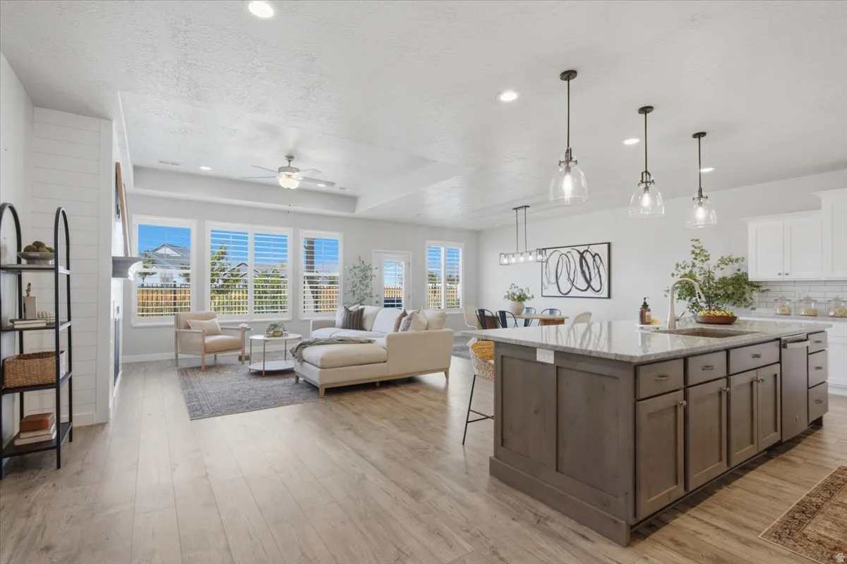 Open-concept living area featuring a kitchen island with stone countertops, wood-finish flooring, a fireplace with shiplap detailing, recessed lighting, and multiple windows with plantation shutters