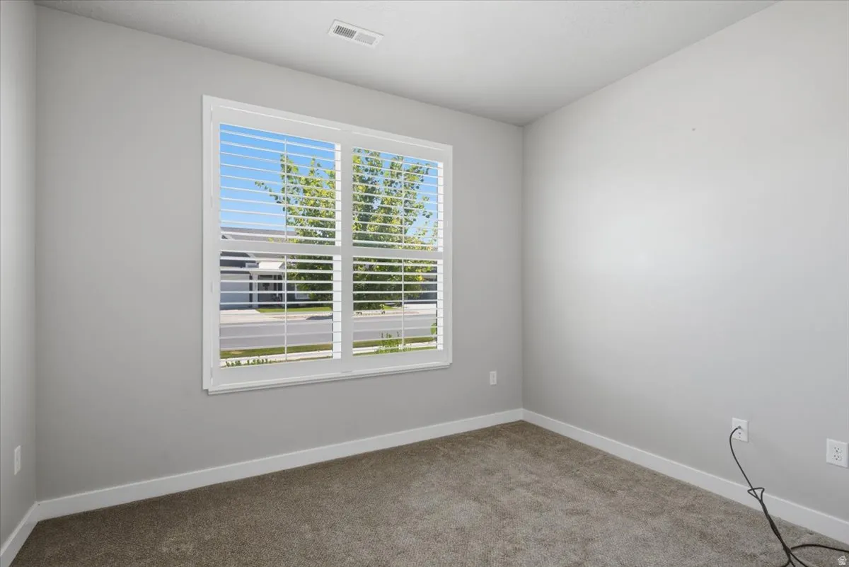Room featuring a large window with white plantation shutters, neutral gray walls, white baseboards, and plush gray carpeting