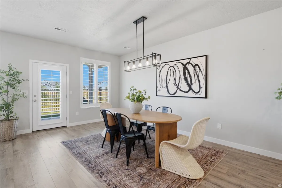 Dining area featuring light wood-finish flooring, a contemporary linear pendant light fixture, and a white single-lite door with exterior access
