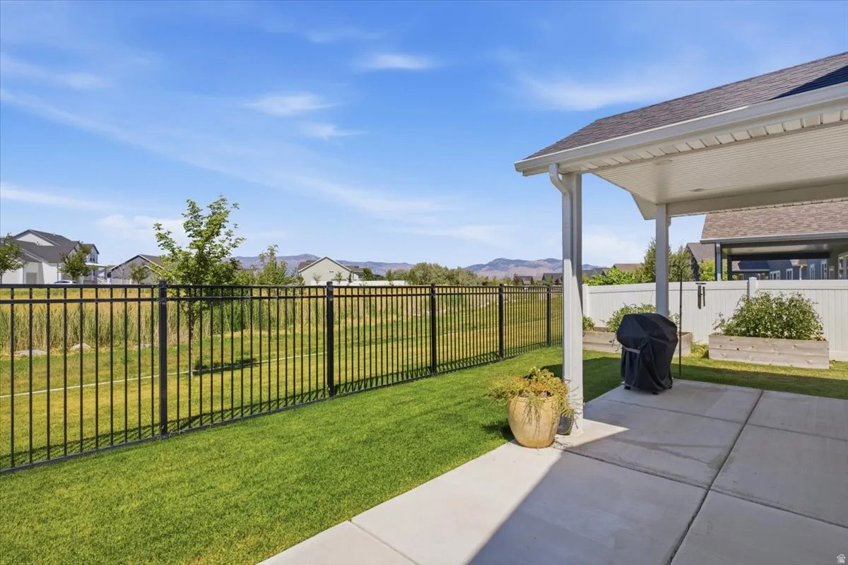 Covered patio with concrete flooring, overlooking a green lawn and black metal fencing