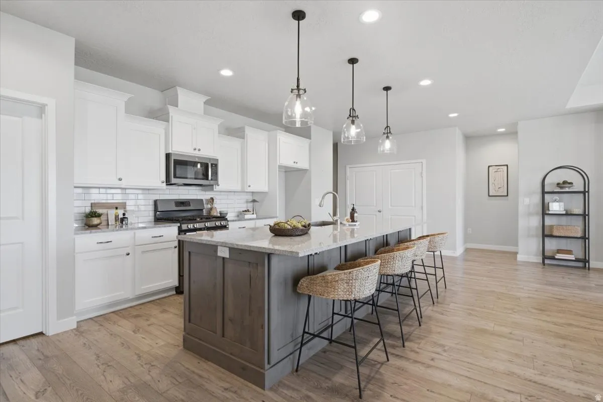 Kitchen featuring a large island with seating, pendant lighting, white cabinetry, subway tile backsplash, and wood-finish flooring