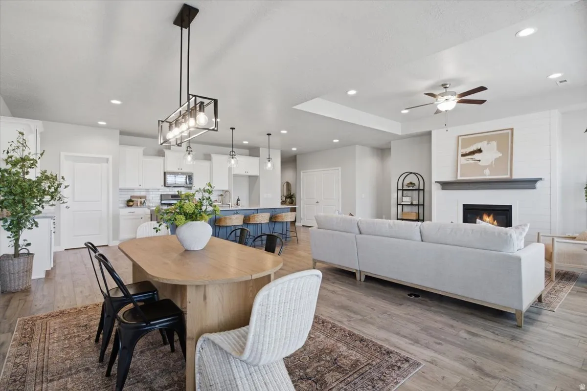 Open-concept living space featuring wood-finish flooring, a contemporary linear chandelier, a kitchen island with seating, a white subway tile backsplash, and a fireplace with a mantel