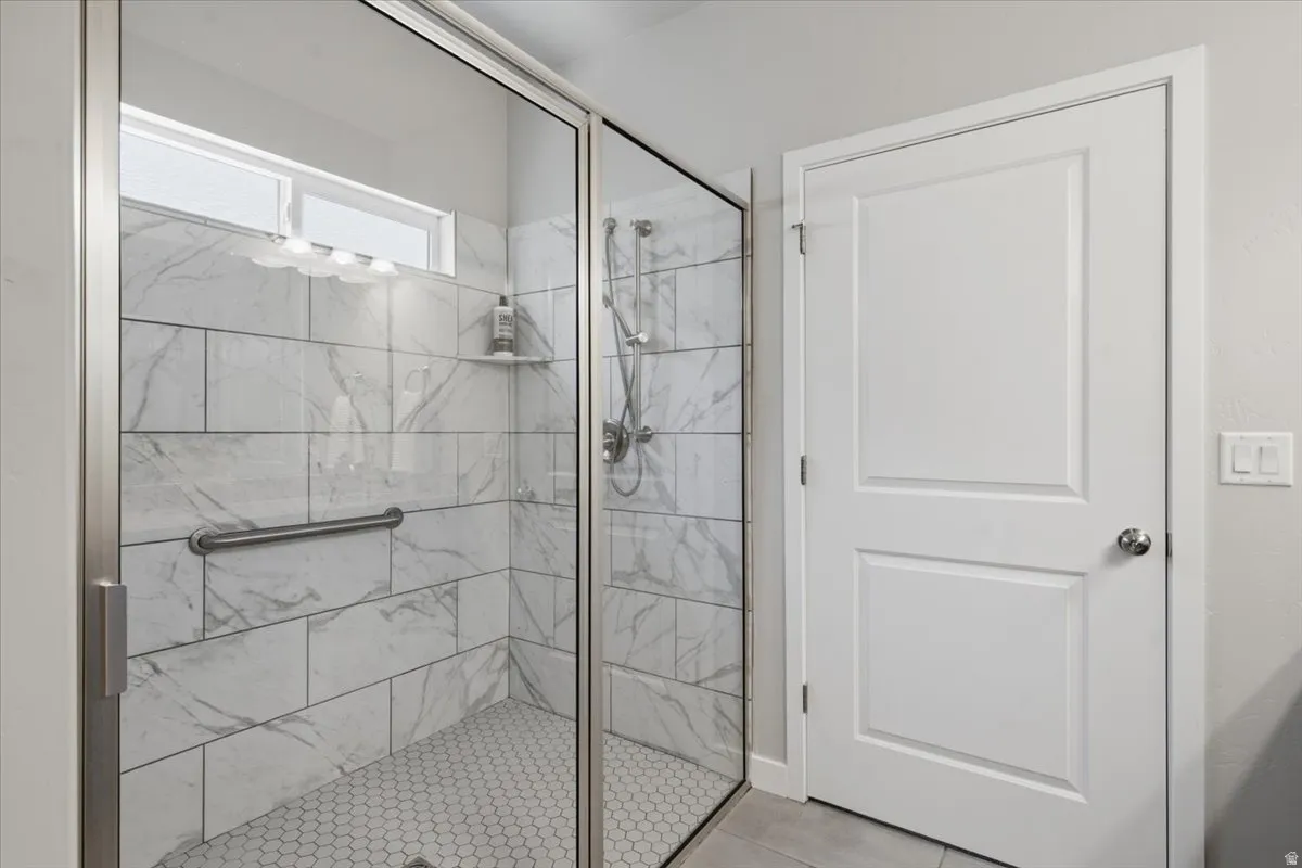 Walk-in shower featuring glass enclosure with brushed nickel hardware, large format marbled wall tiles, hexagonal floor tiles, and an integrated grab bar