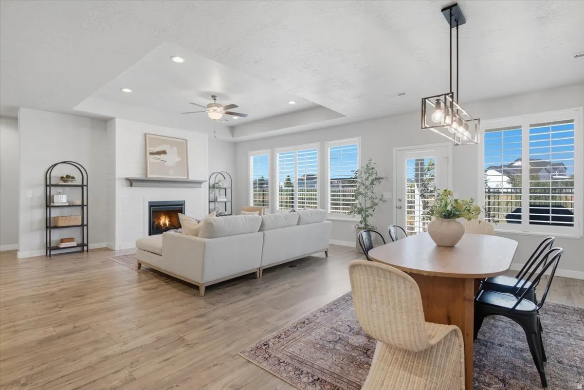 Open-concept living space featuring wood-finish flooring, a white brick fireplace with a mantel, and a tray ceiling with recessed lighting