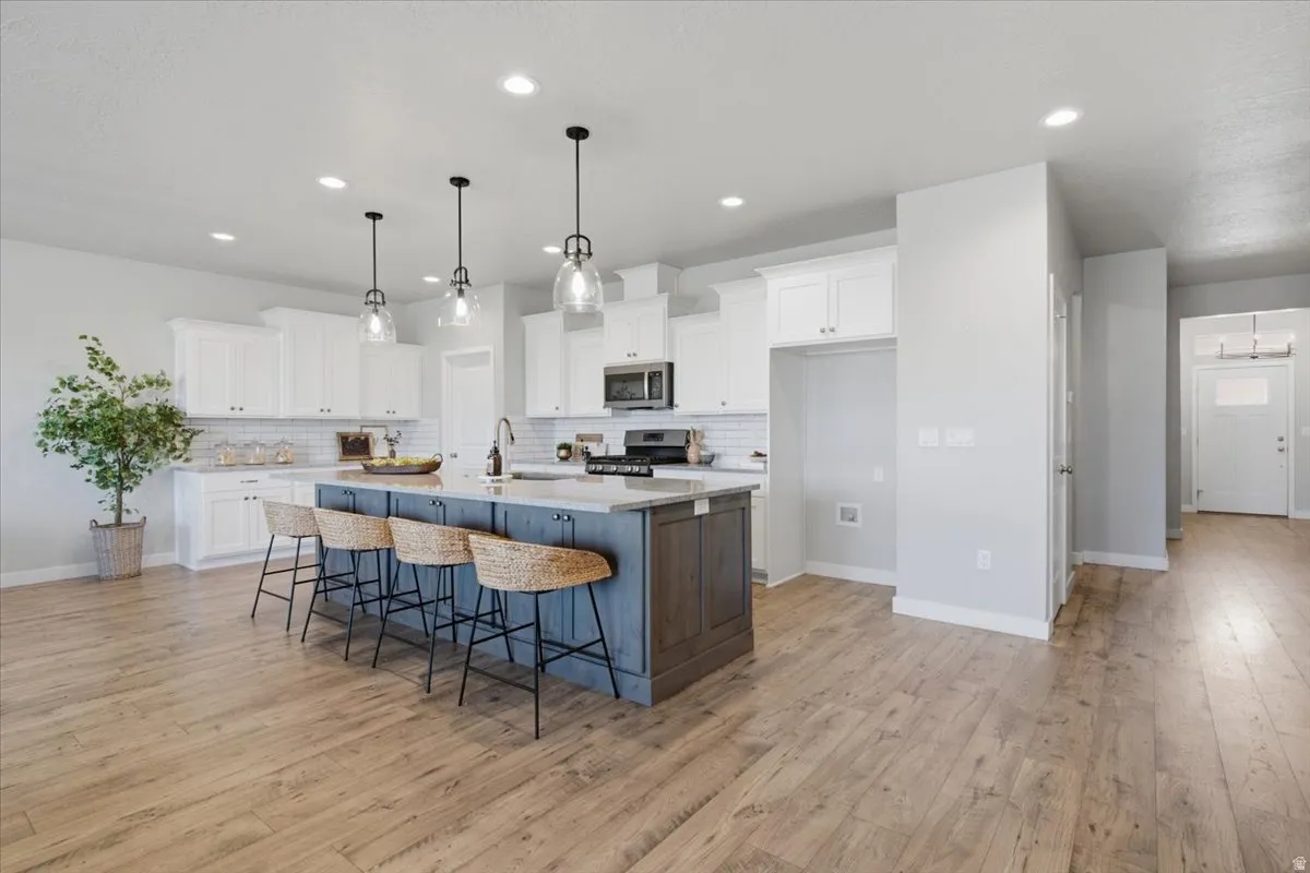 Open-concept kitchen featuring an island with pendant lighting, white shaker cabinetry, stainless steel appliances, subway tile backsplash, and wood-finish flooring