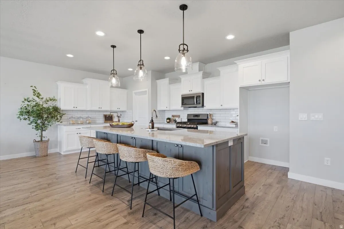 Spacious kitchen featuring an oversized island with pendant lighting, stone countertops, white cabinetry, subway tile backsplash, and wood-finish flooring