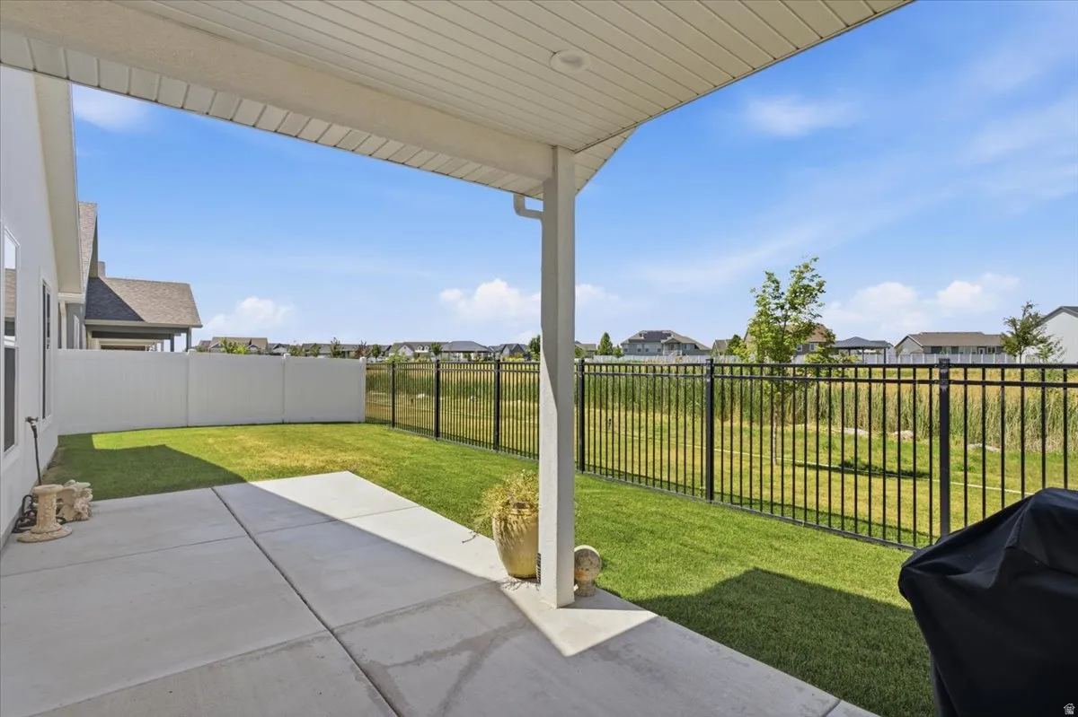 Covered patio with a concrete surface, featuring a manicured lawn, white privacy fencing, and black wrought iron fencing